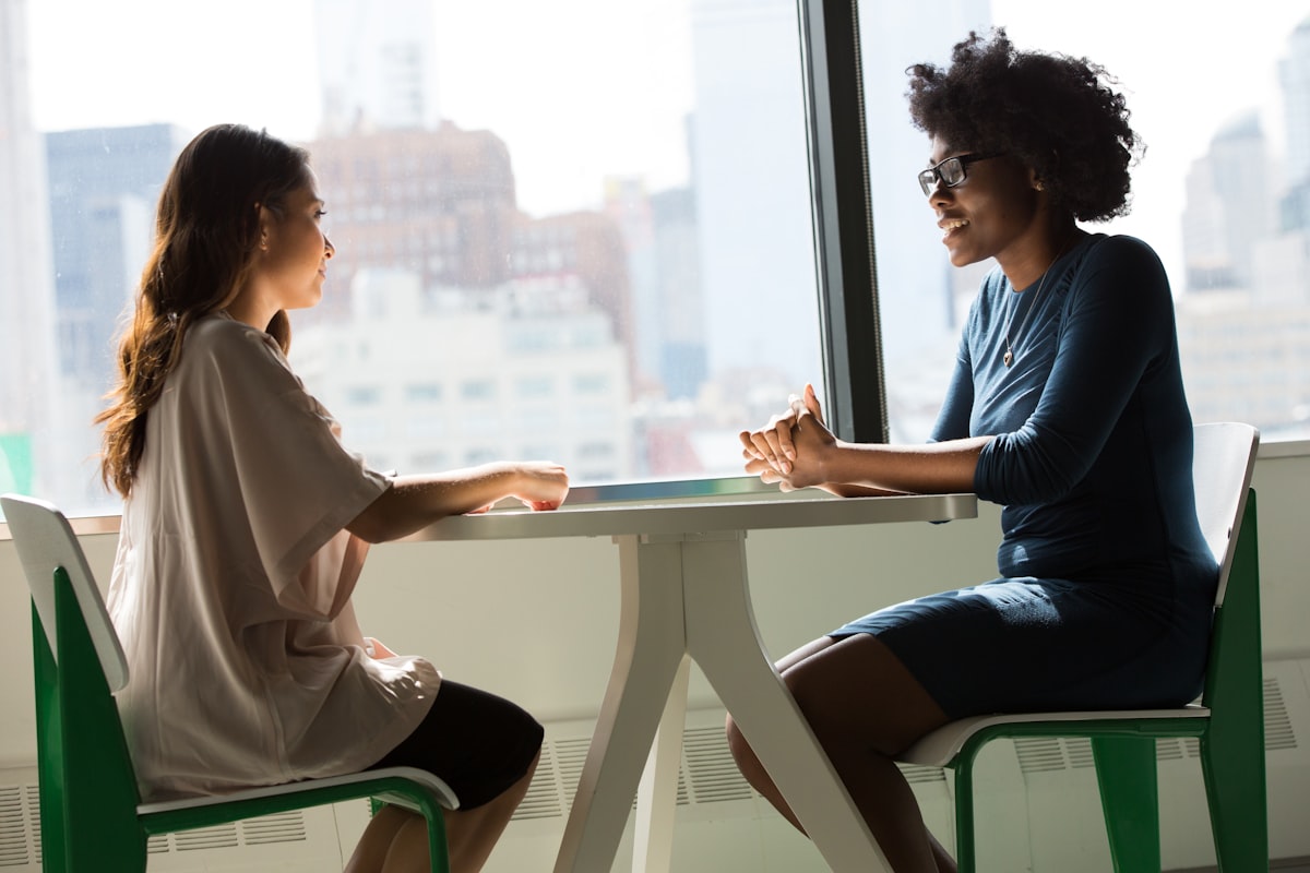 Two women sitting beside a table and talking, representing mentoring and capability building